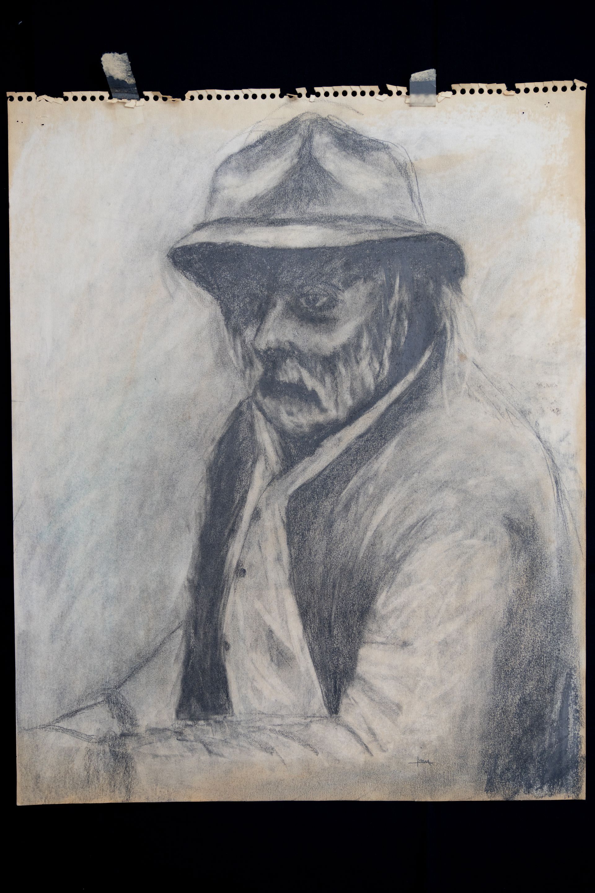 Charcoal drawing of a person wearing a hat and coat, looking down.