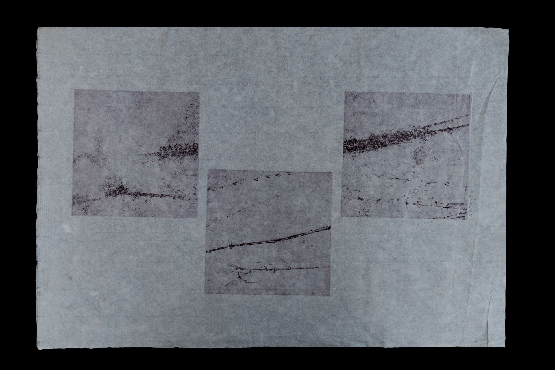 Three dark square panels on a grey rectangular paper. Each panel contains blurry, dark markings resembling lines or textures.