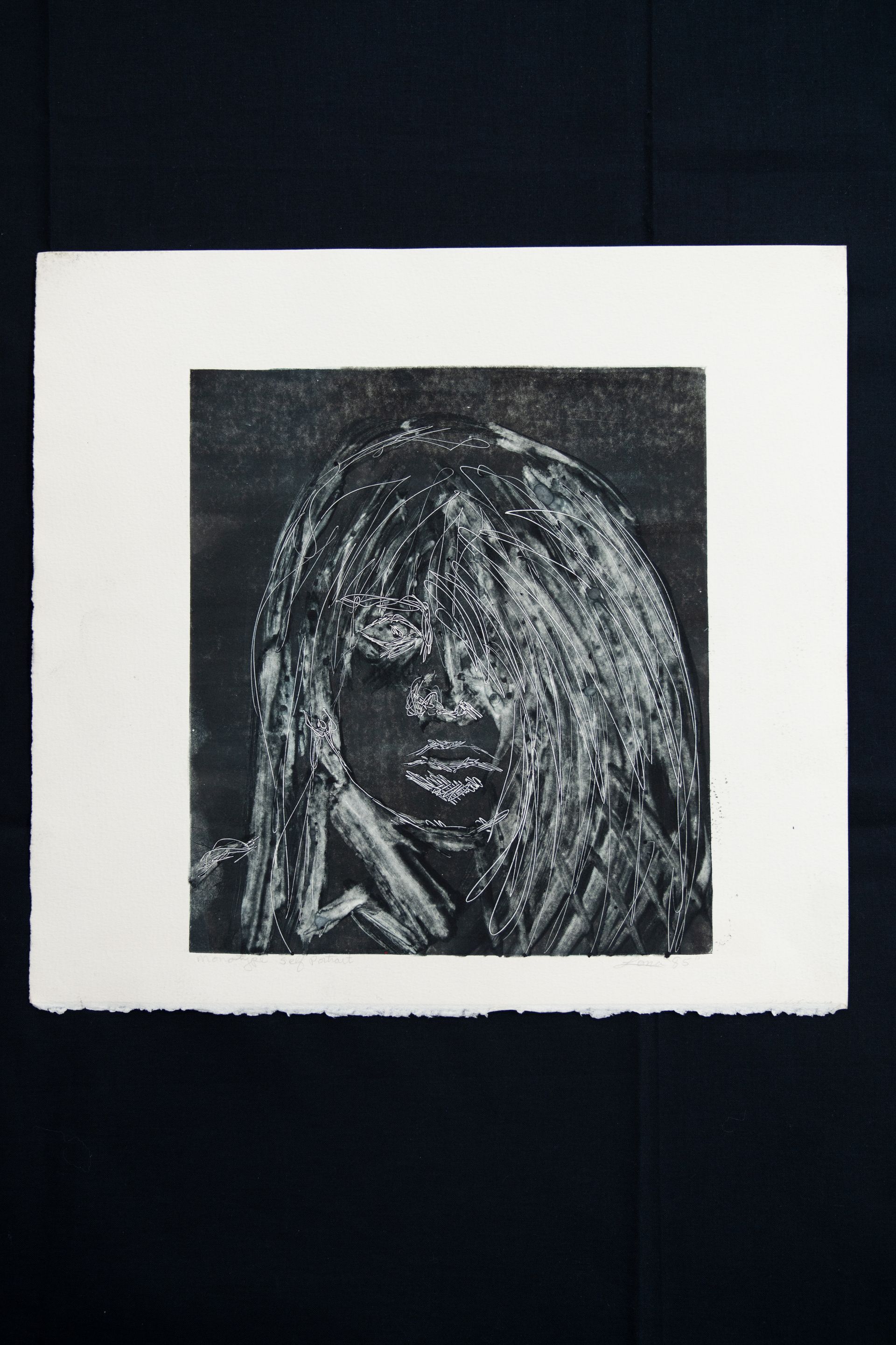 Monochrome print of a person with long hair, hand to face, in a square frame on white paper.
