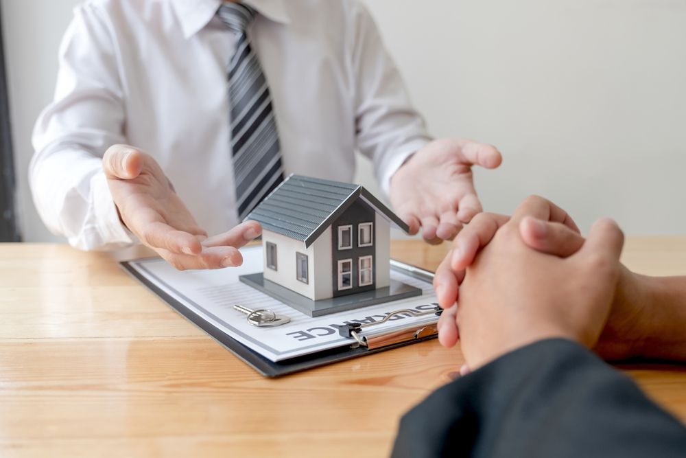 A man is holding a model house in his hands while sitting at a table .
