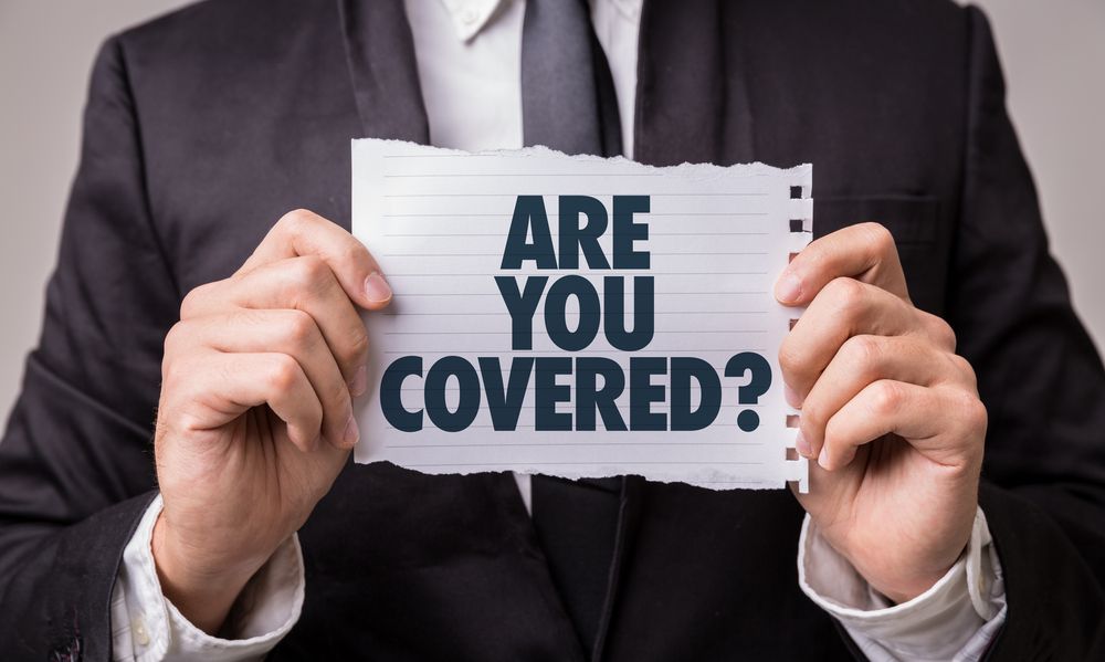 A man in a suit and tie is holding a piece of paper that says `` are you covered '' .