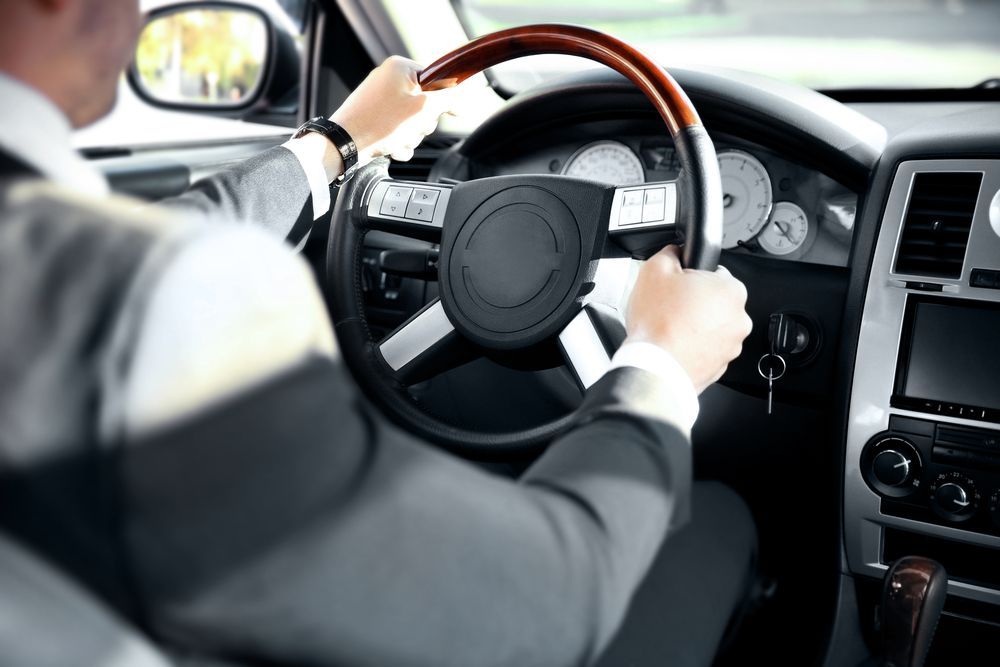 a man in a suit is driving a car with a wooden steering wheel .