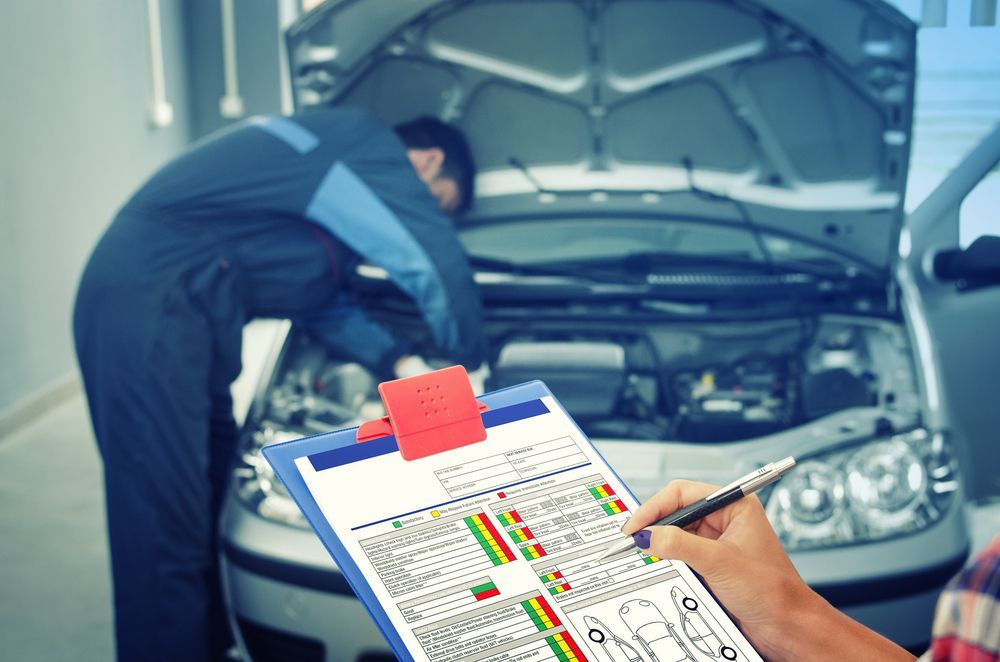 A man is writing on a clipboard while a mechanic works on a car .
