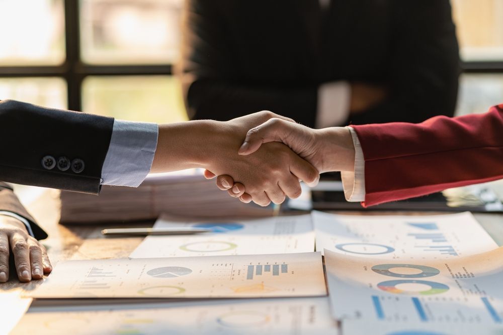 A man and a woman are shaking hands over a table .
