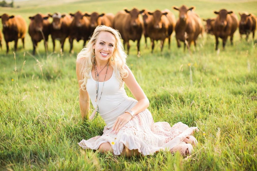 A woman is kneeling in the grass in front of a herd of cows.