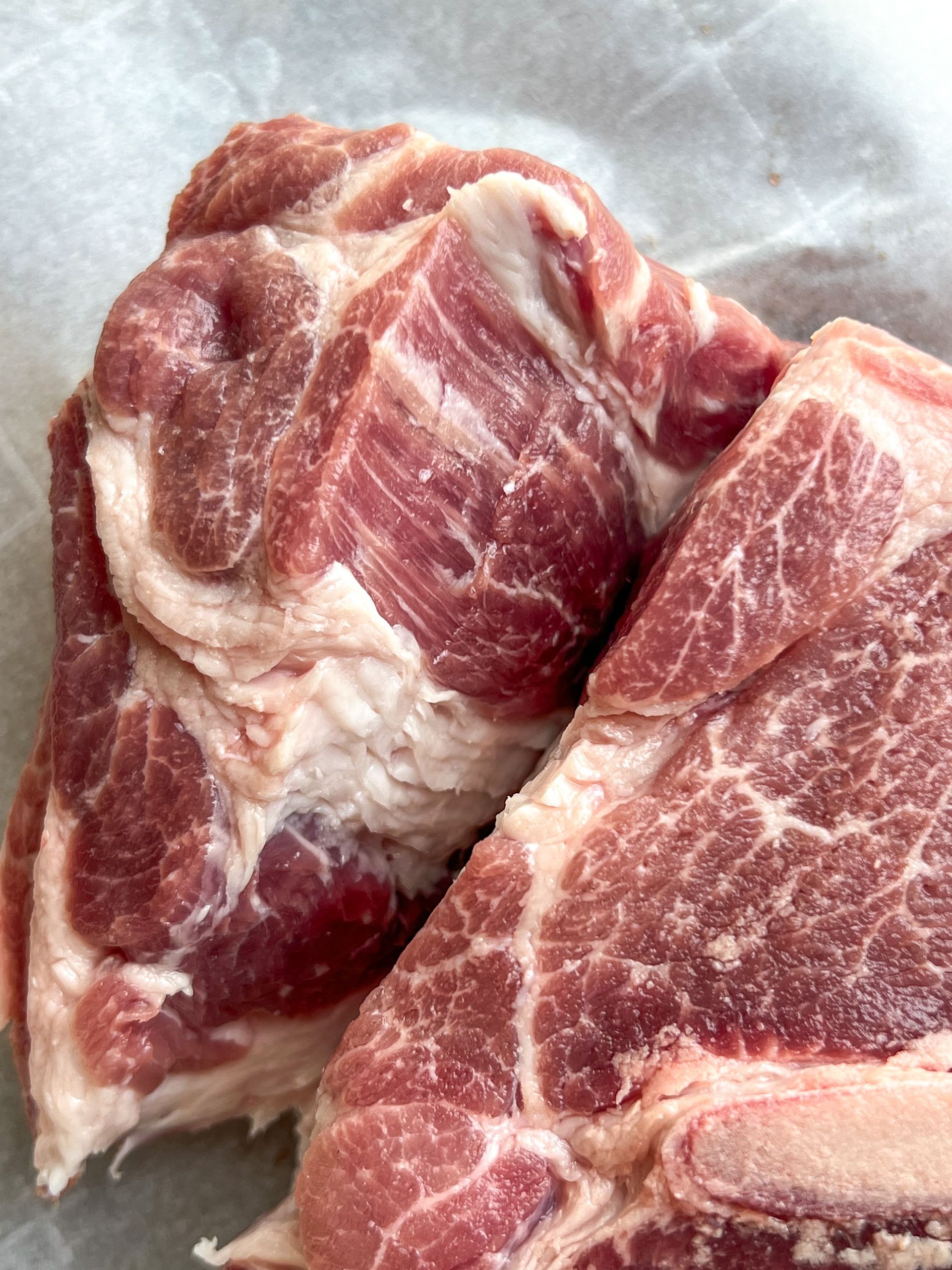 Two pieces of raw meat are sitting on a piece of wax paper