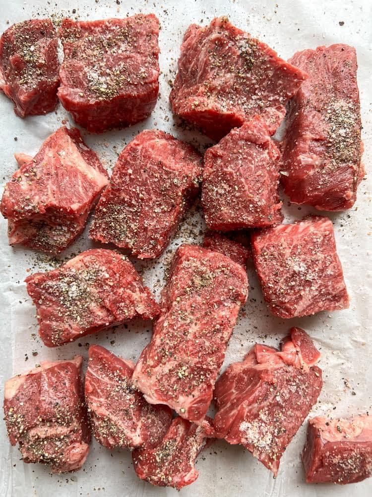 A pile of beef cubes covered in pepper on a piece of wax paper.