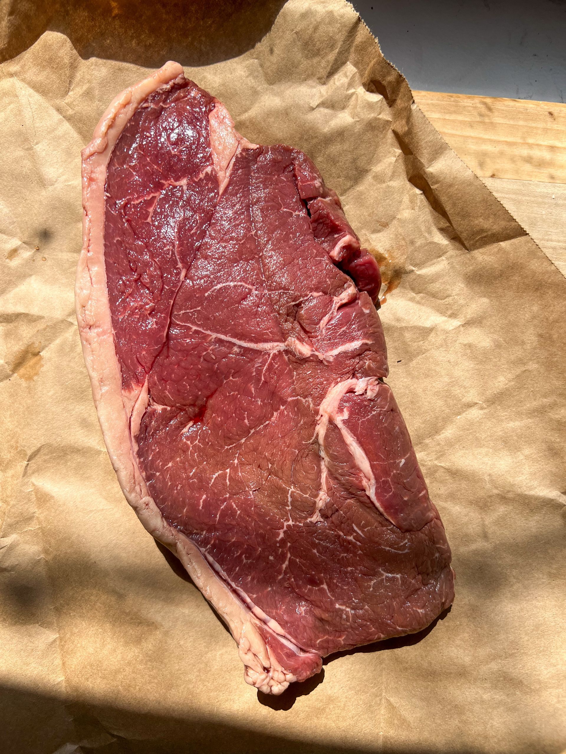 A piece of raw steak is sitting on a piece of brown paper.