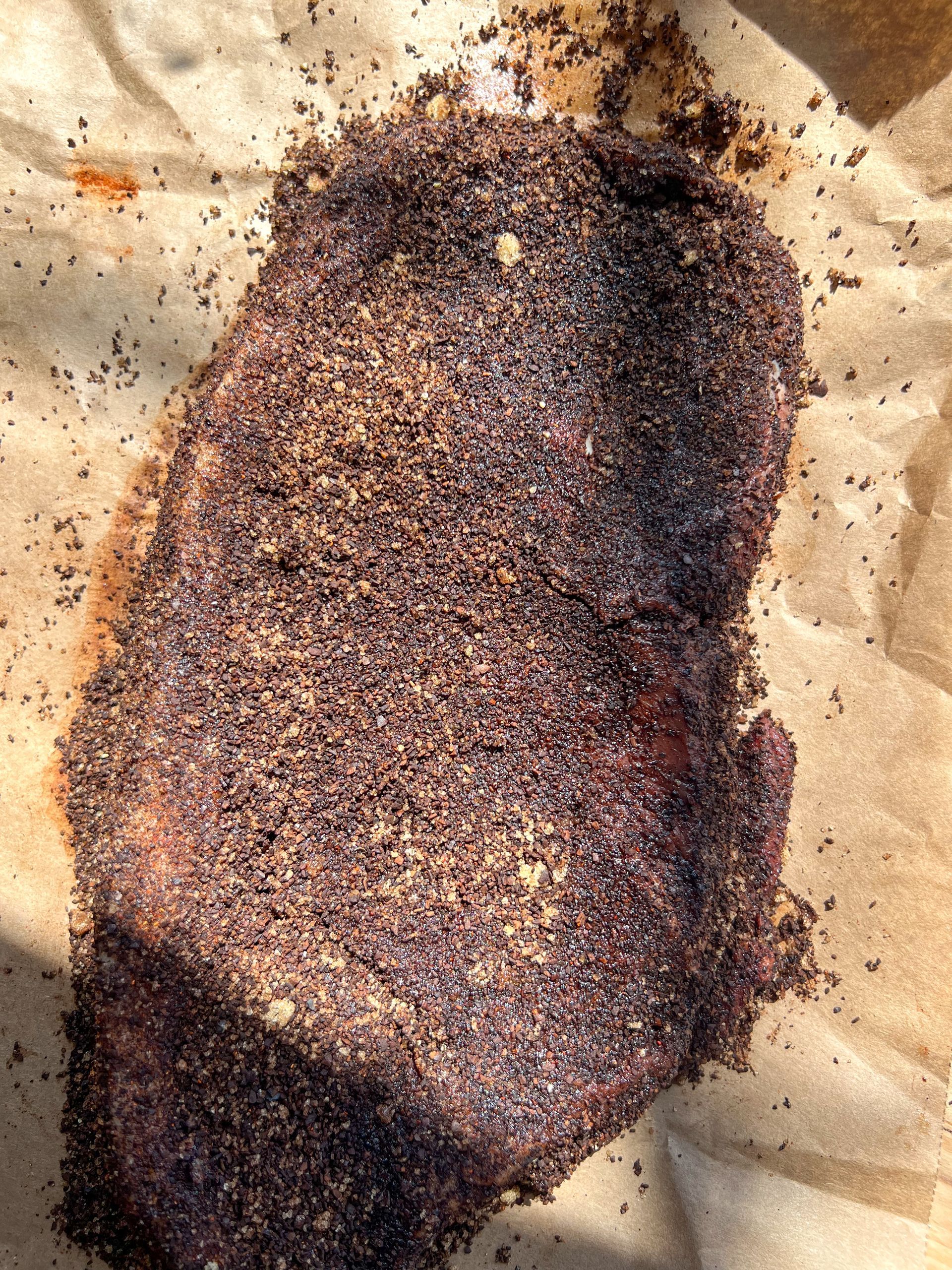 A piece of meat is covered in powdered spices on a piece of paper.