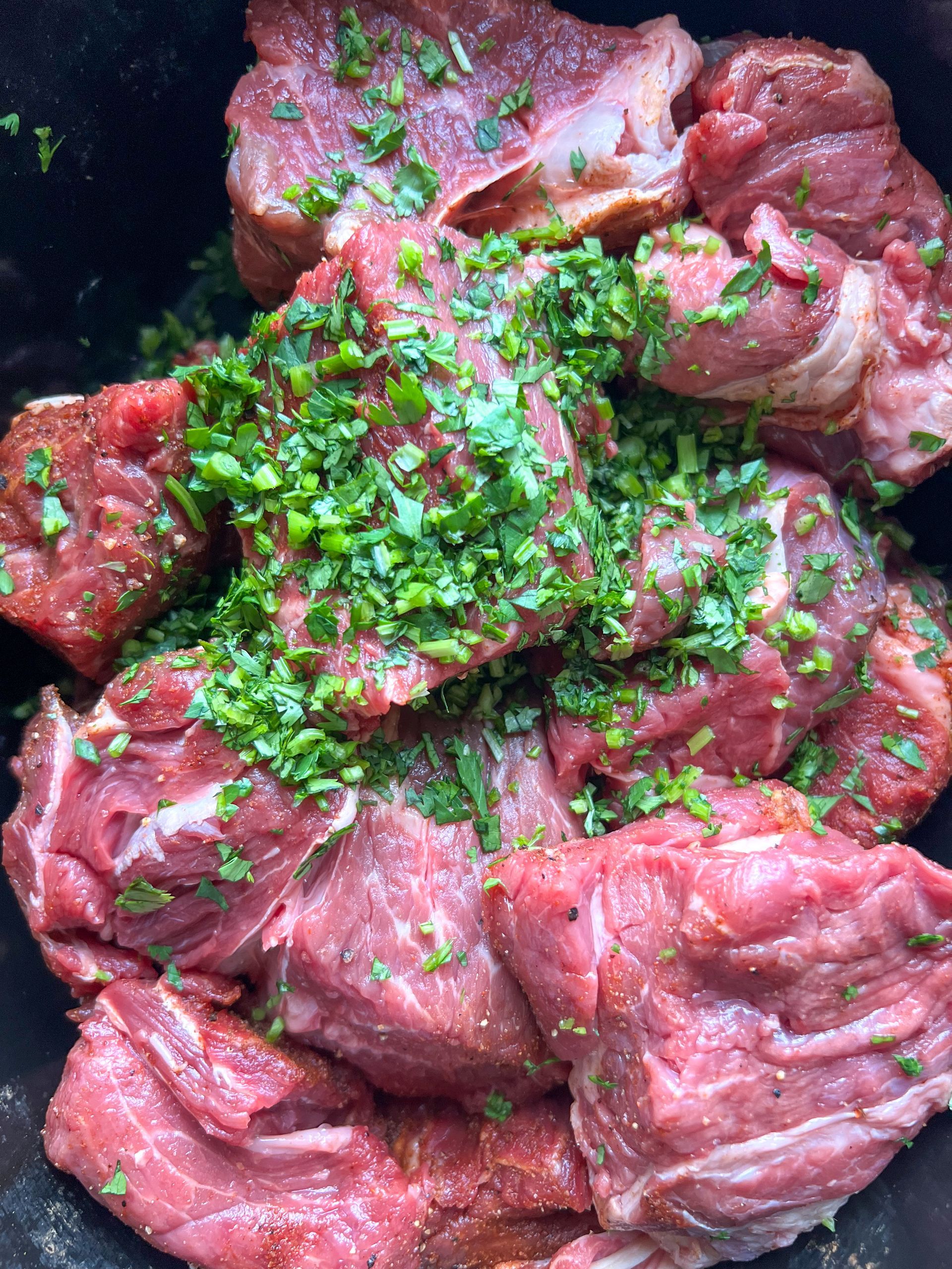 A close up of a pile of raw meat with herbs on top.