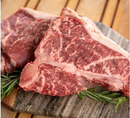 Two raw t-bones are sitting on a wooden cutting board.