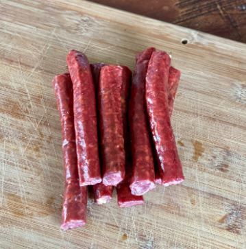 A bunch of sausage sticks are sitting on top of a wooden cutting board.