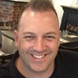 A man is smiling for the camera while sitting at a table in a restaurant.