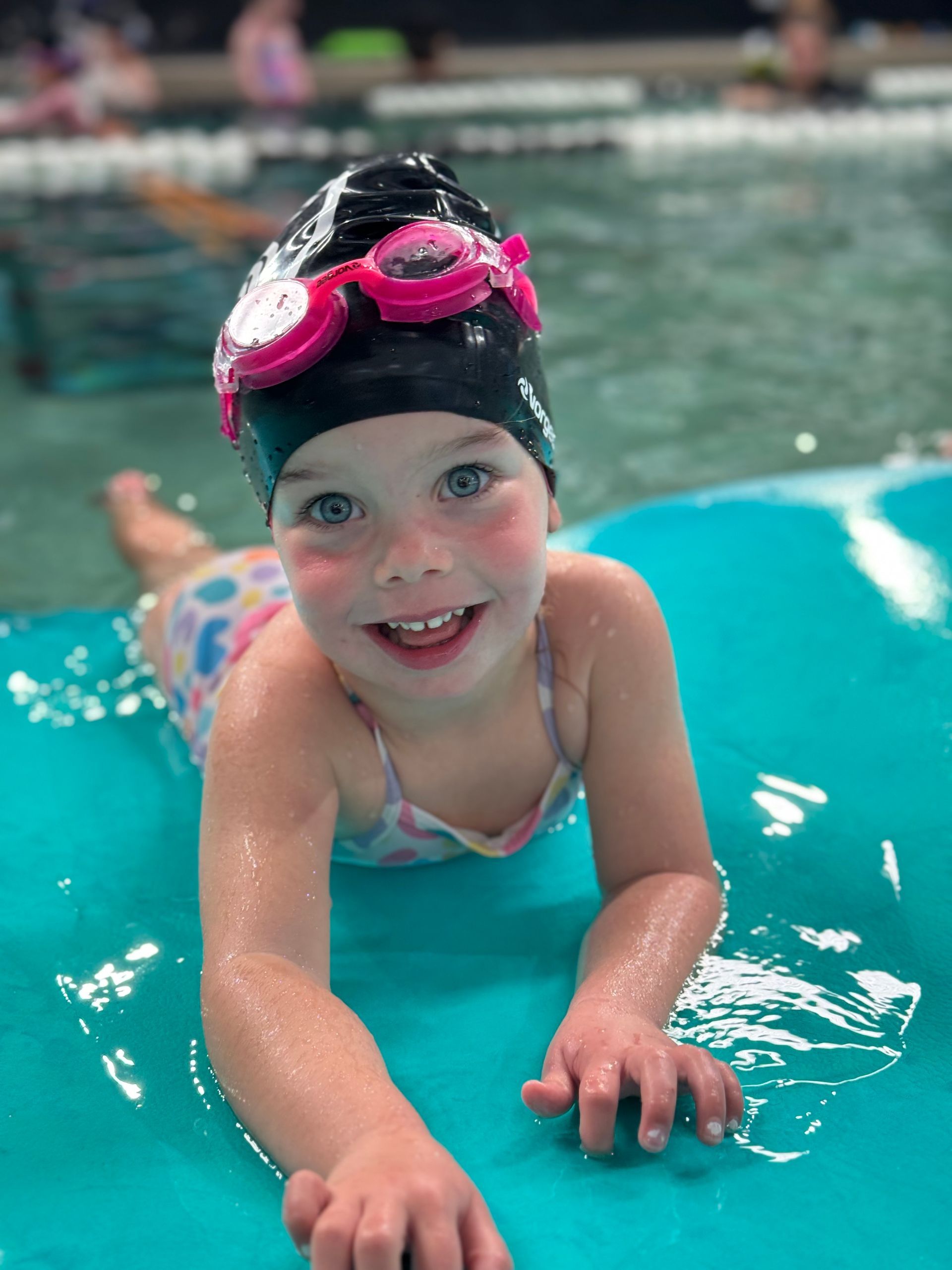 A little girl wearing a swim cap and goggles is swimming in a pool.