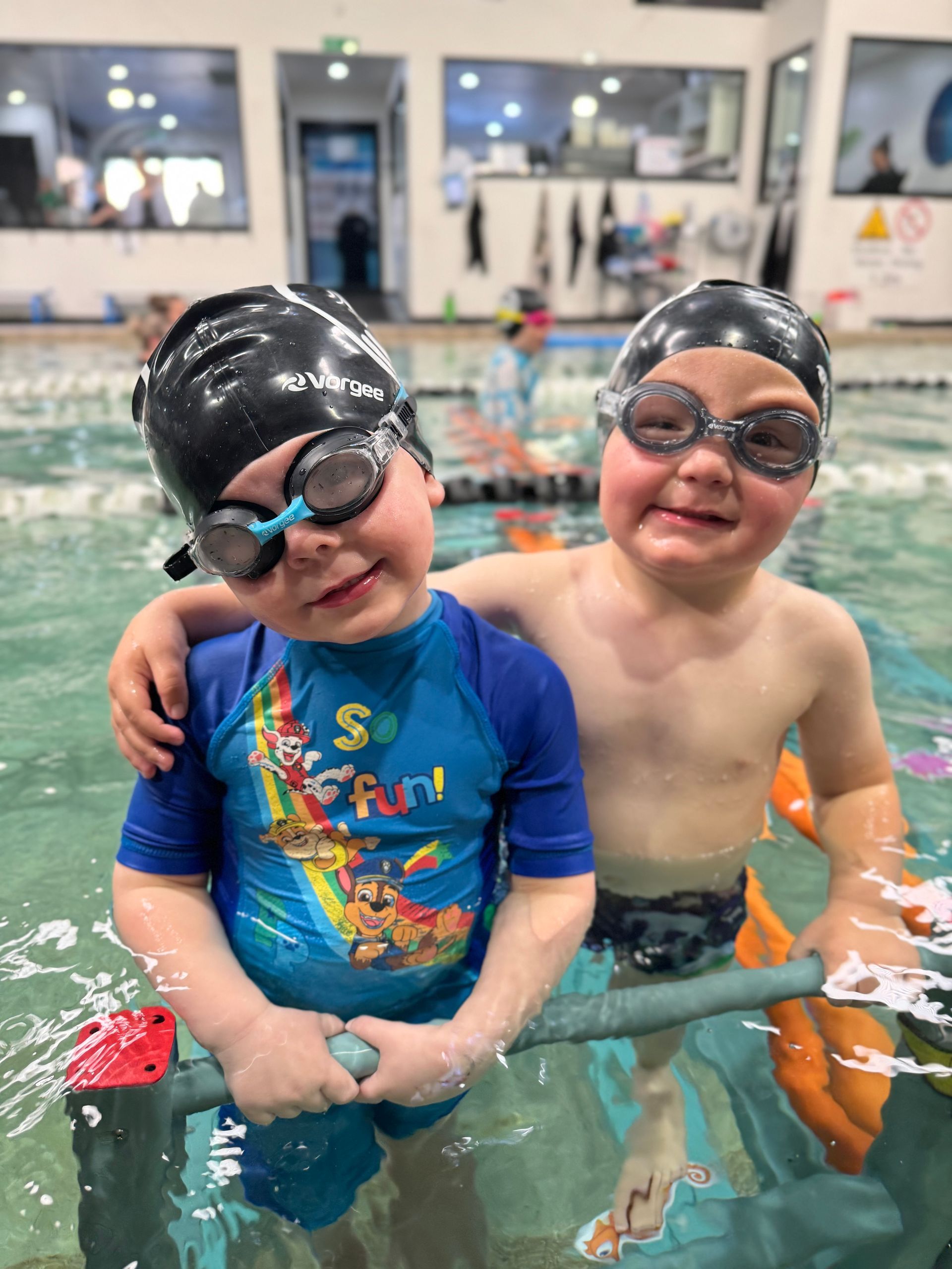 Two young boys are standing next to each other in a swimming pool.