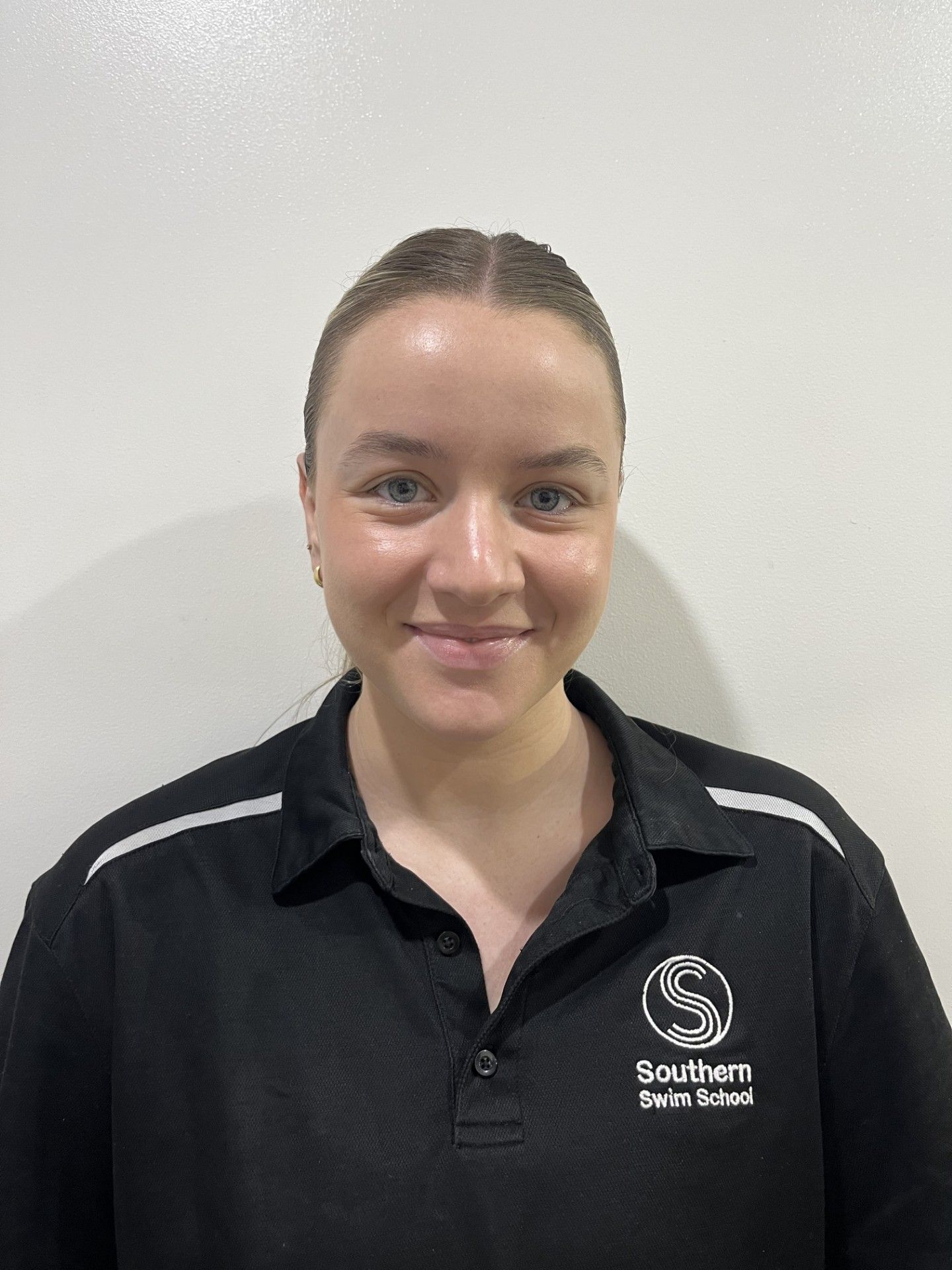 A young woman wearing a black polo shirt is smiling for the camera.