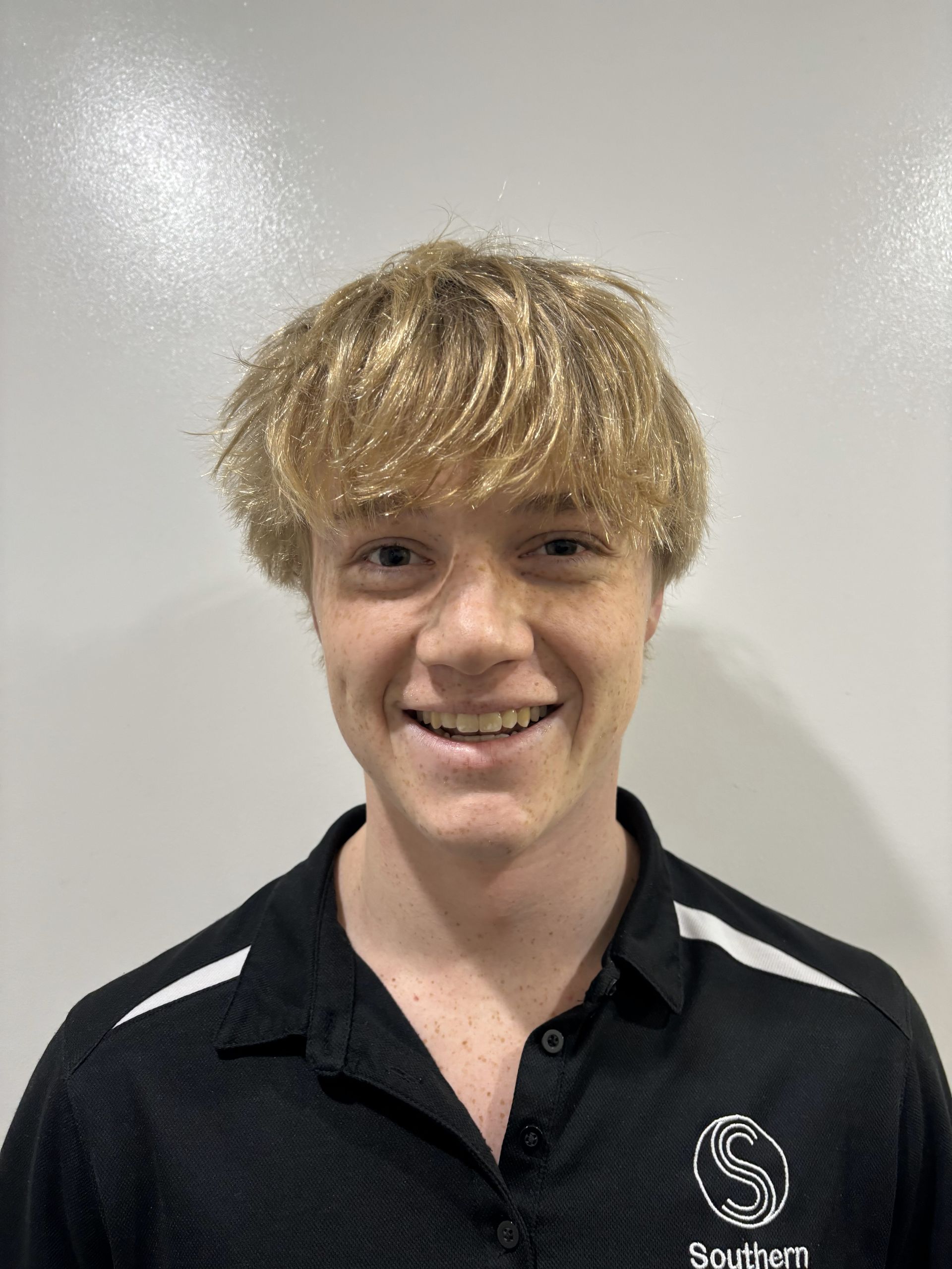 A young man with blonde hair is wearing a black shirt and smiling.