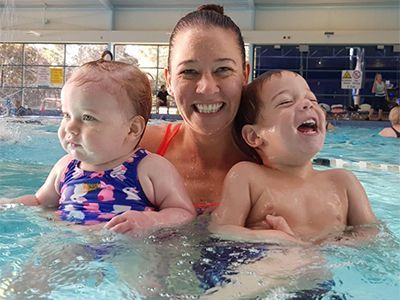 A woman is holding two babies in a swimming pool.