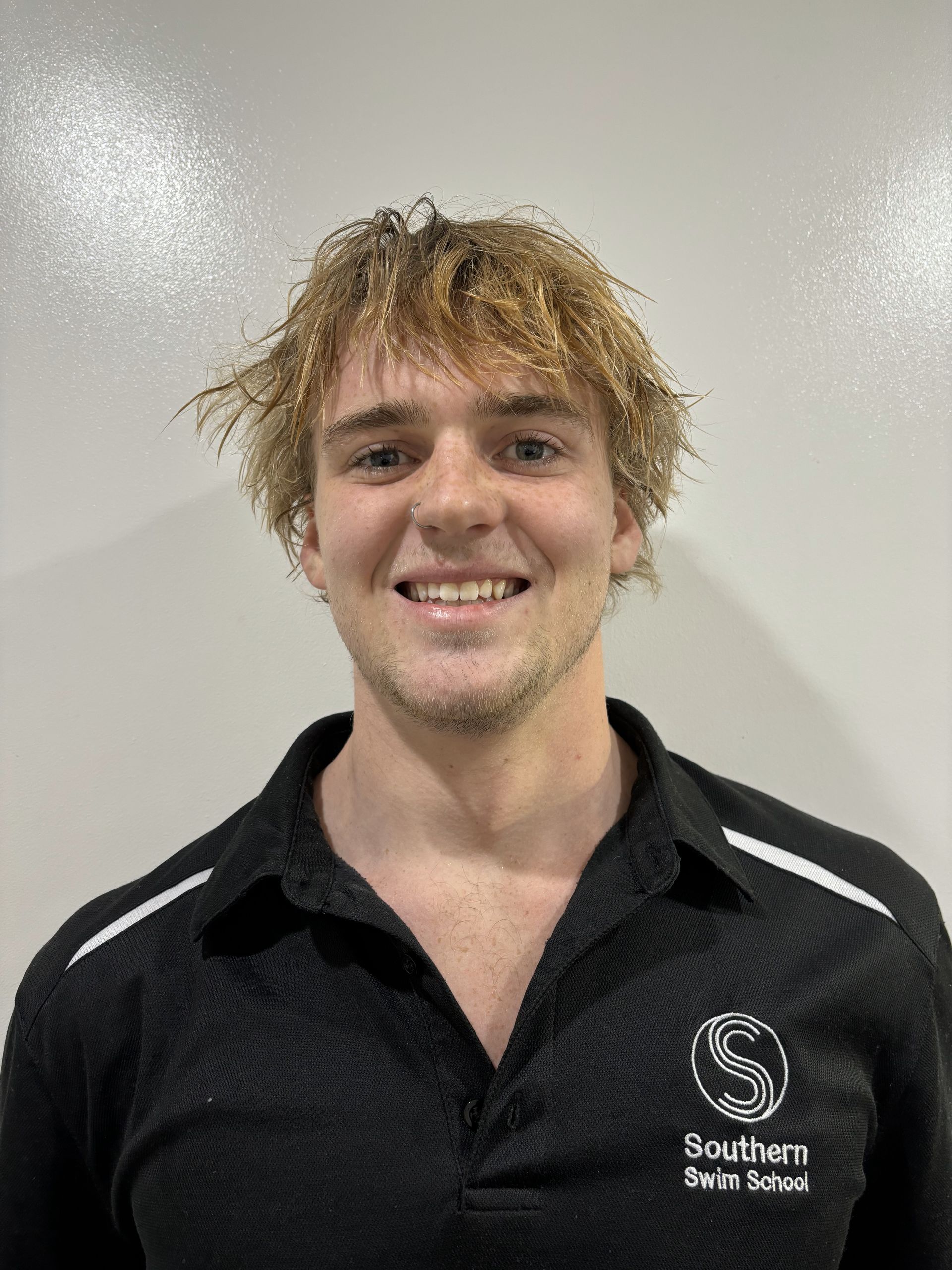 A young man with blonde hair is wearing a black shirt and smiling.