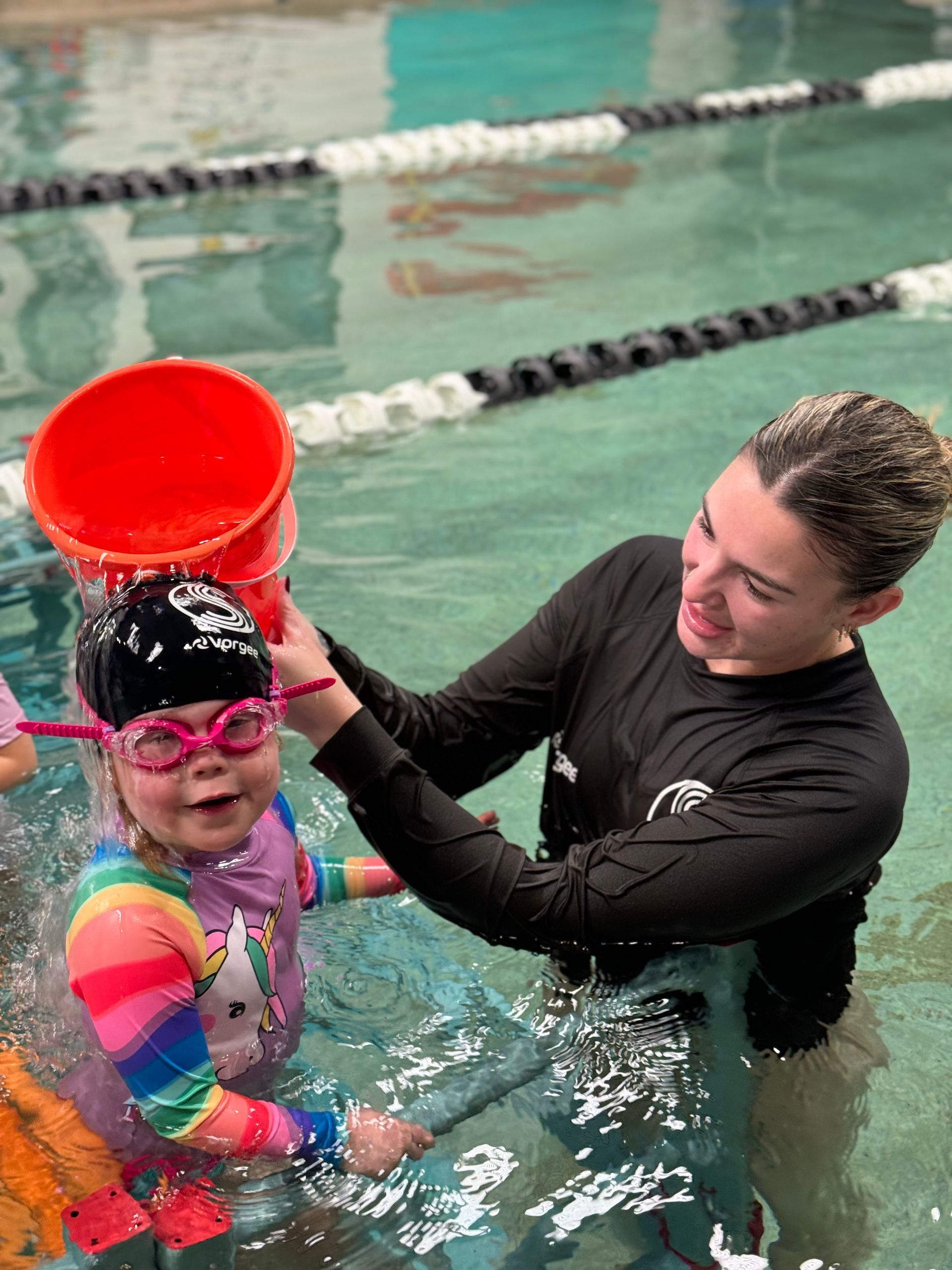 A woman is teaching a little girl how to swim in a swimming pool.