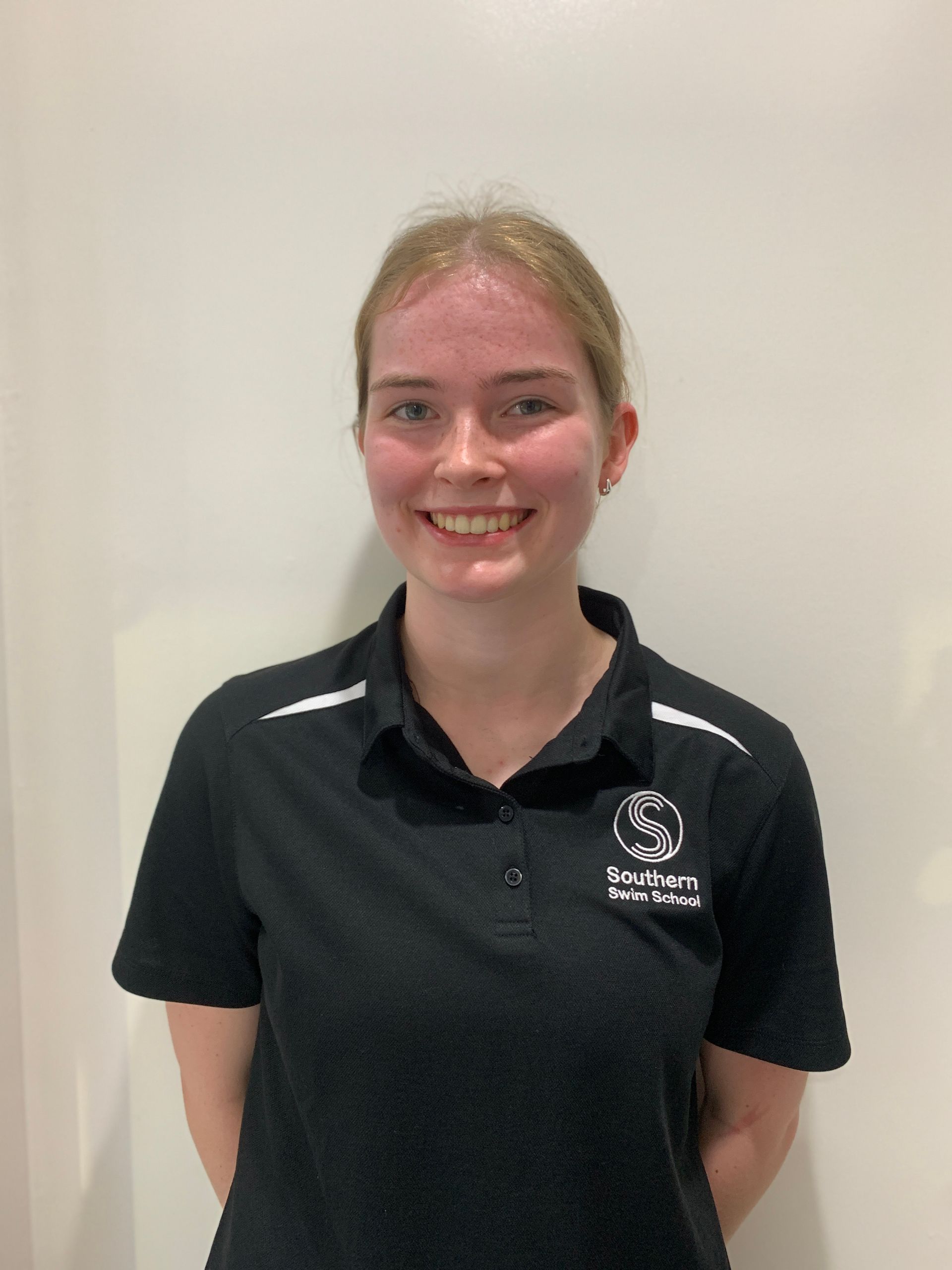 A young woman wearing a black polo shirt is smiling for the camera.