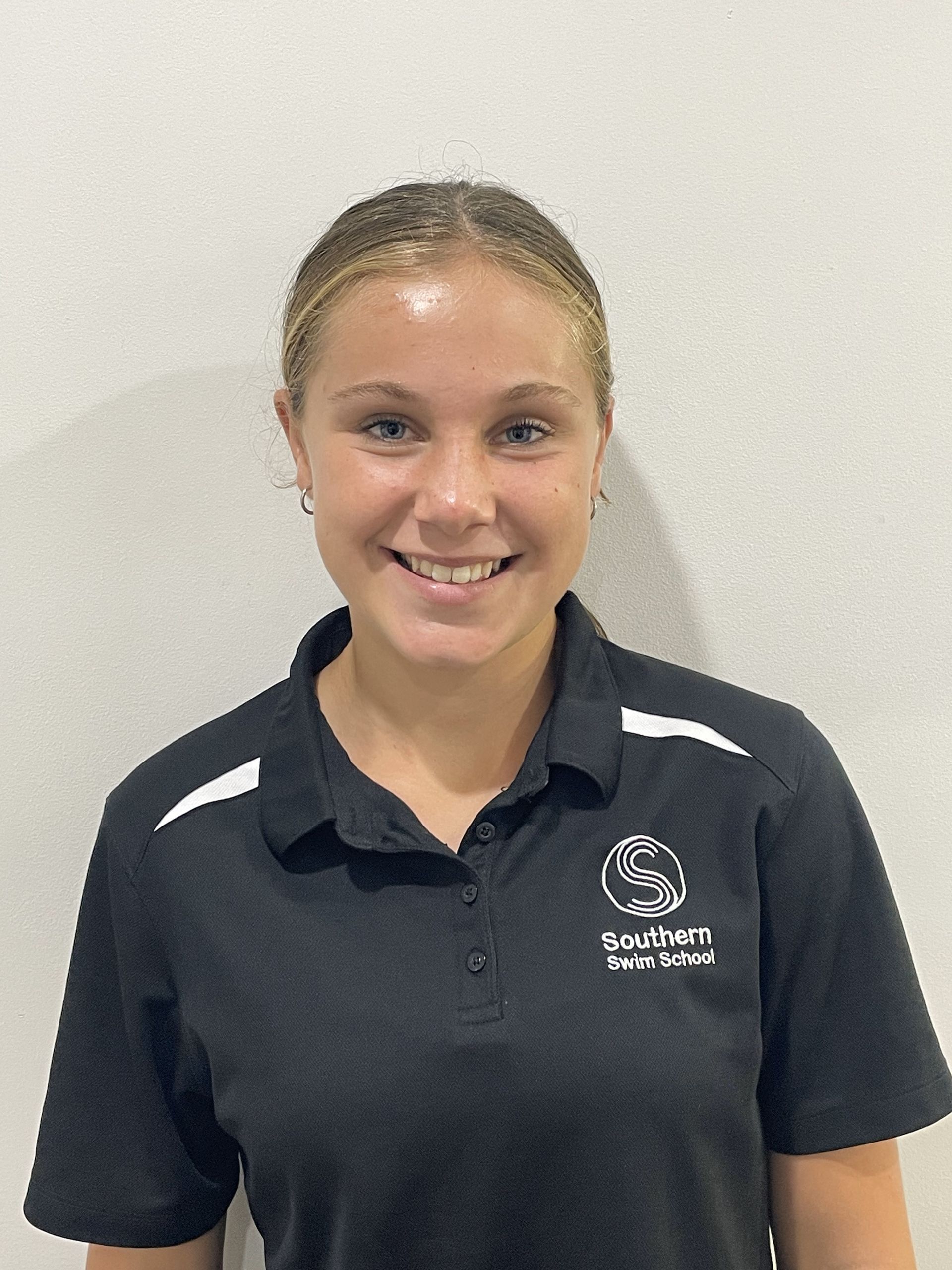 A young woman wearing a black polo shirt is smiling for the camera.