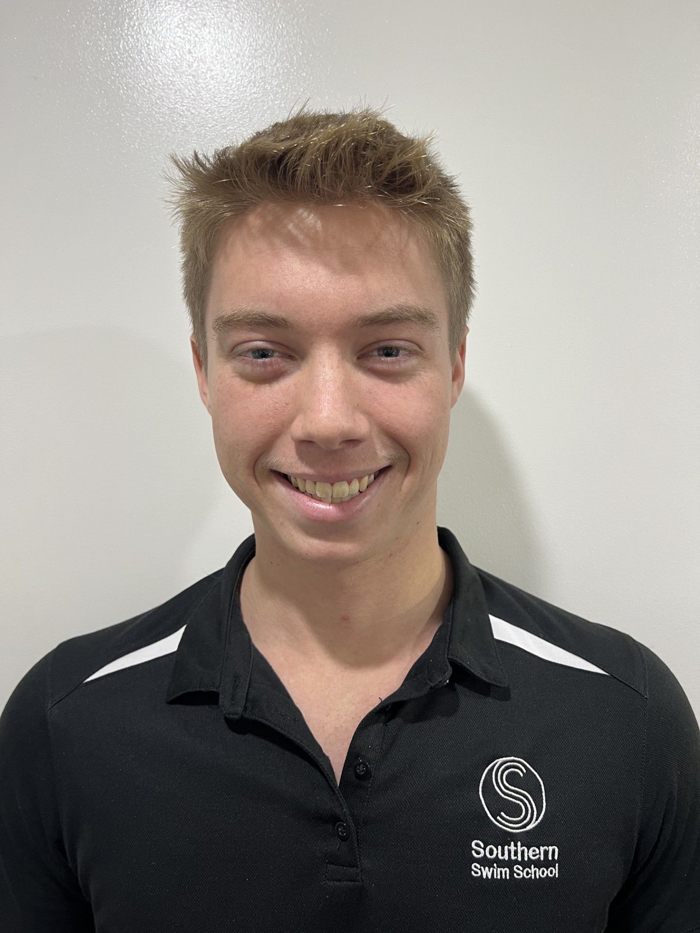 A young man wearing a black polo shirt is smiling for the camera.