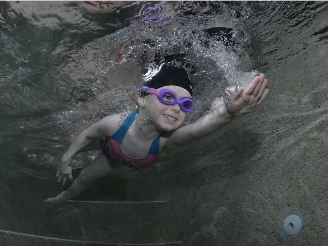 A young girl wearing goggles and a swim cap is swimming underwater
