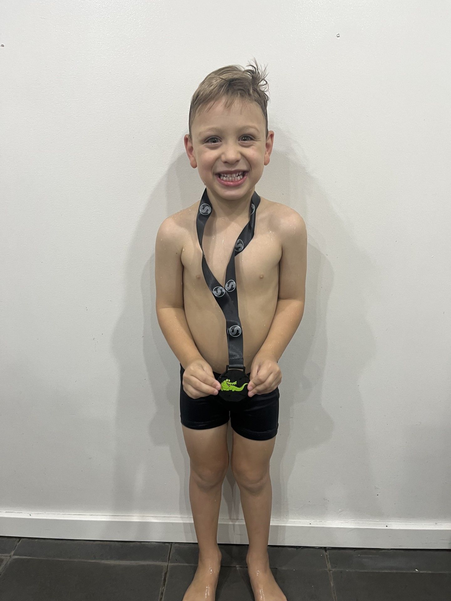 A young boy without a shirt is holding a medal around his neck.