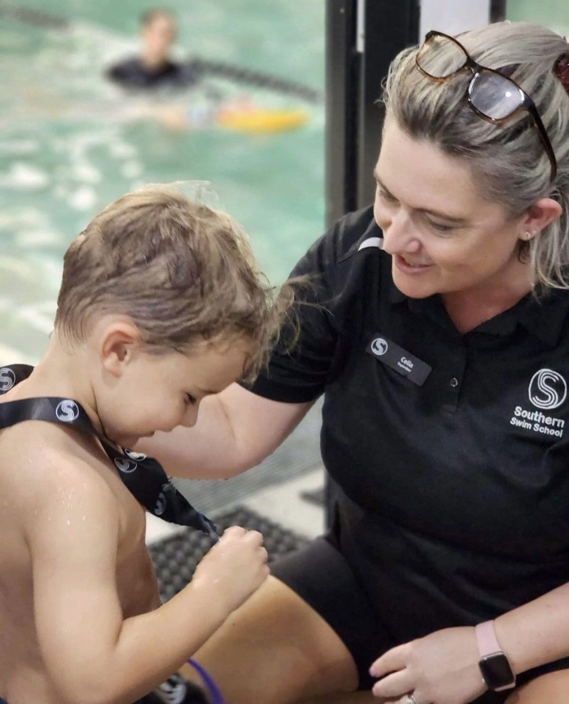 A woman is sitting next to a young boy in a swimming pool.