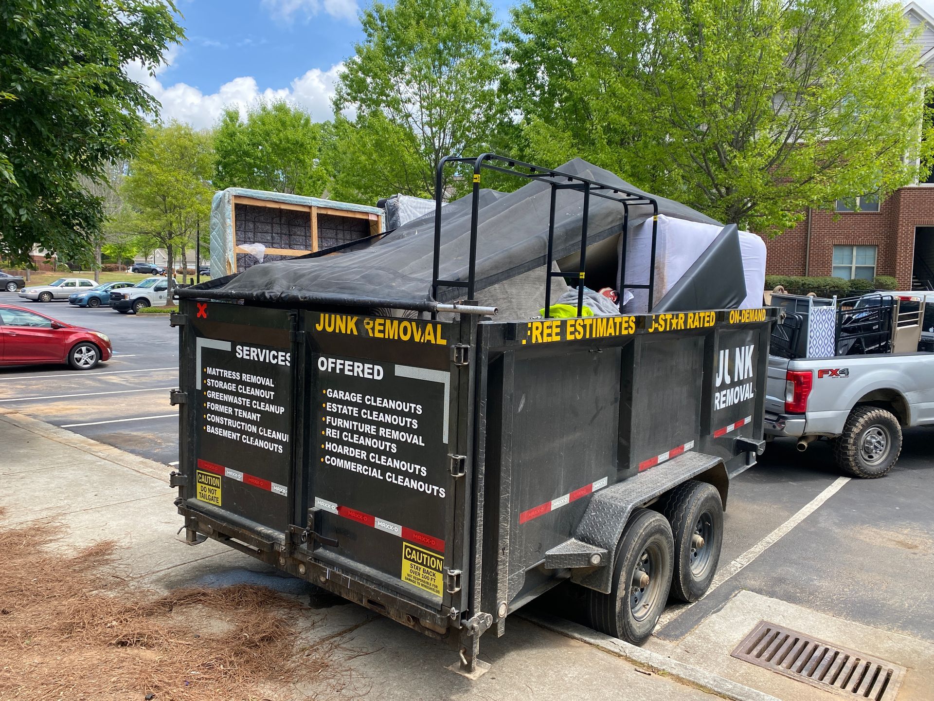 A dumpster trailer is parked in a parking lot next to a truck.