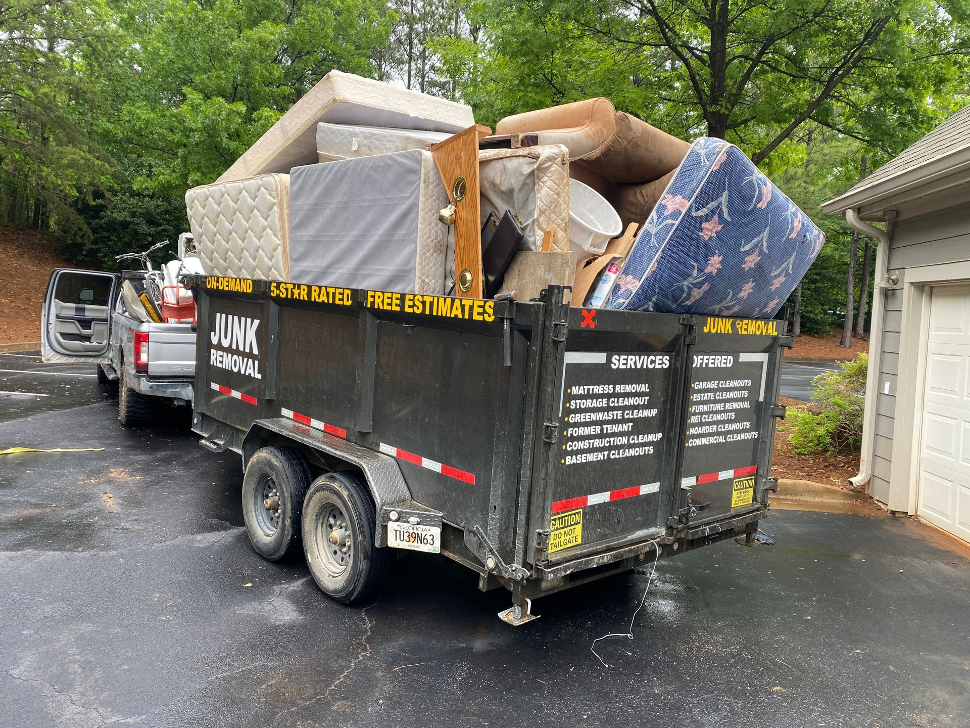 A trailer filled with junk is parked in front of a garage.