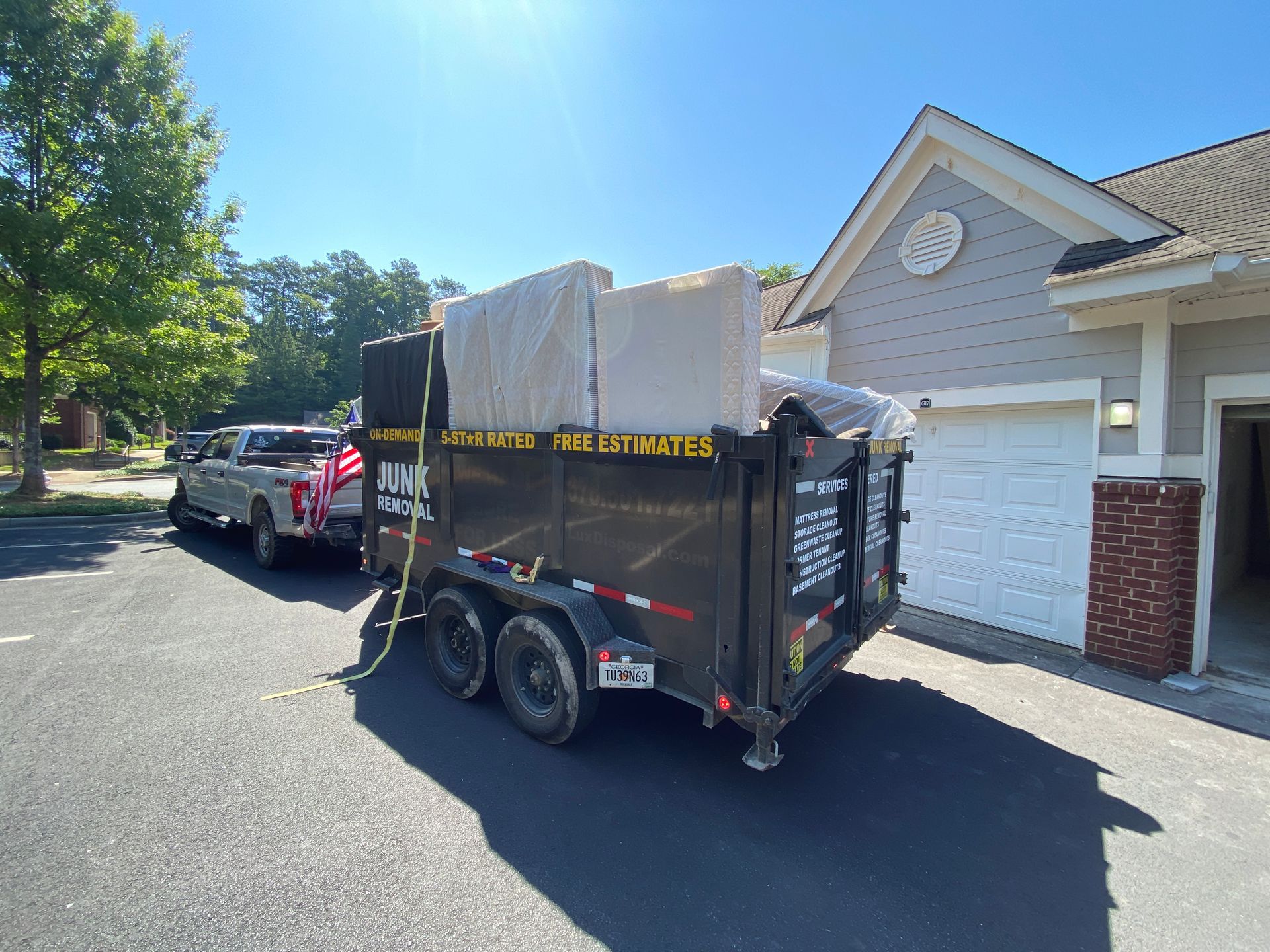 A dumpster is being towed by a truck in front of a house.