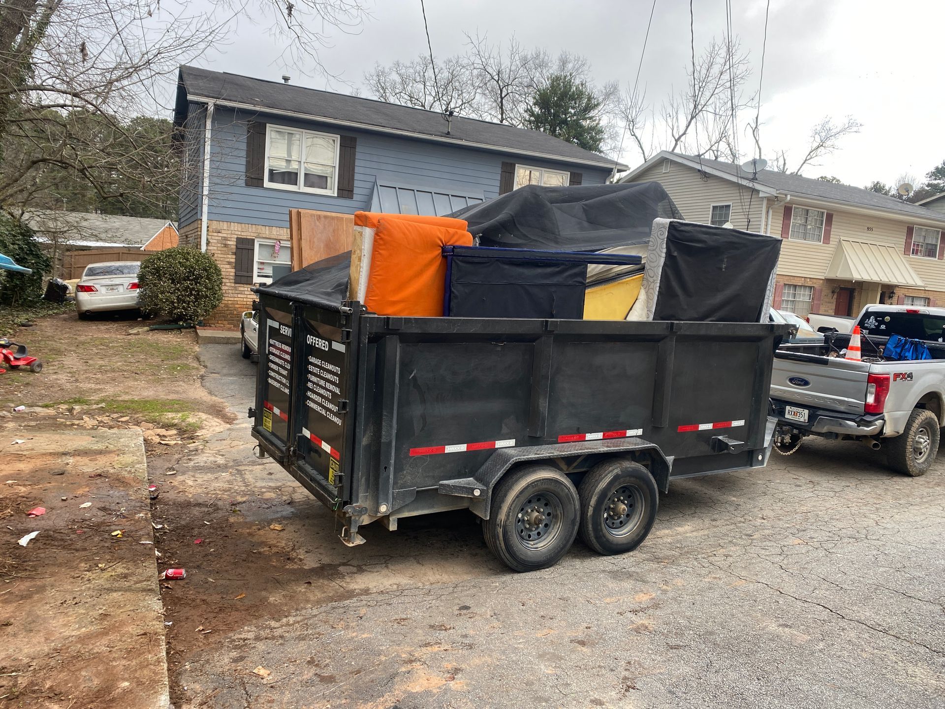 A dumpster trailer filled with junk is parked in front of a house.