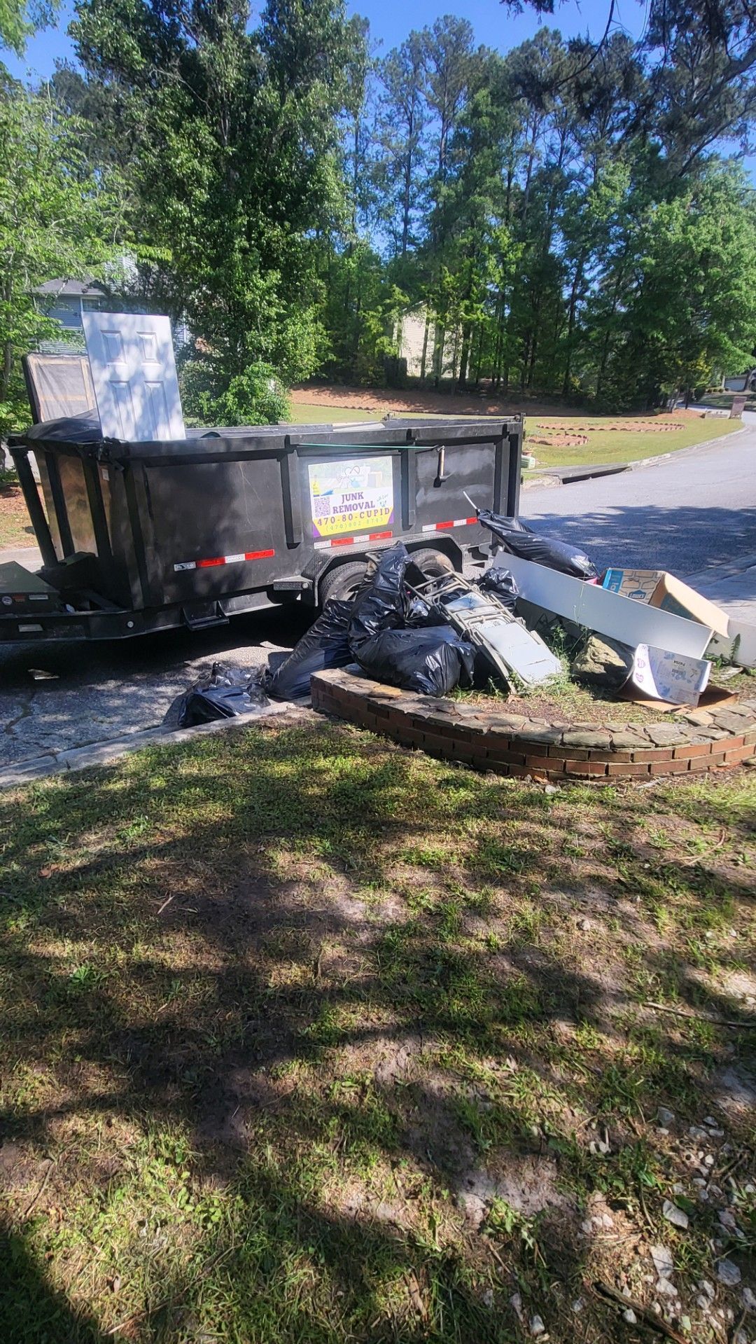 A dumpster is sitting in the grass next to a brick wall.