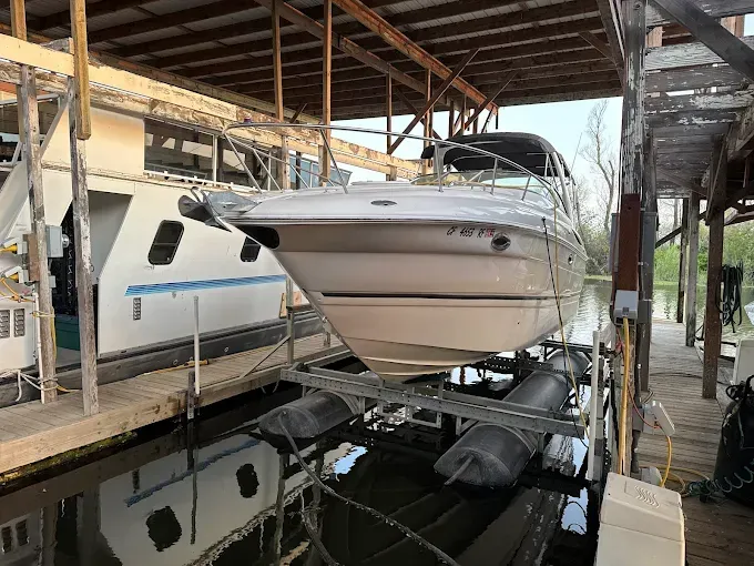 Boat on a lift in a boathouse, viewed head-on. Water, dock, and another boat visible.