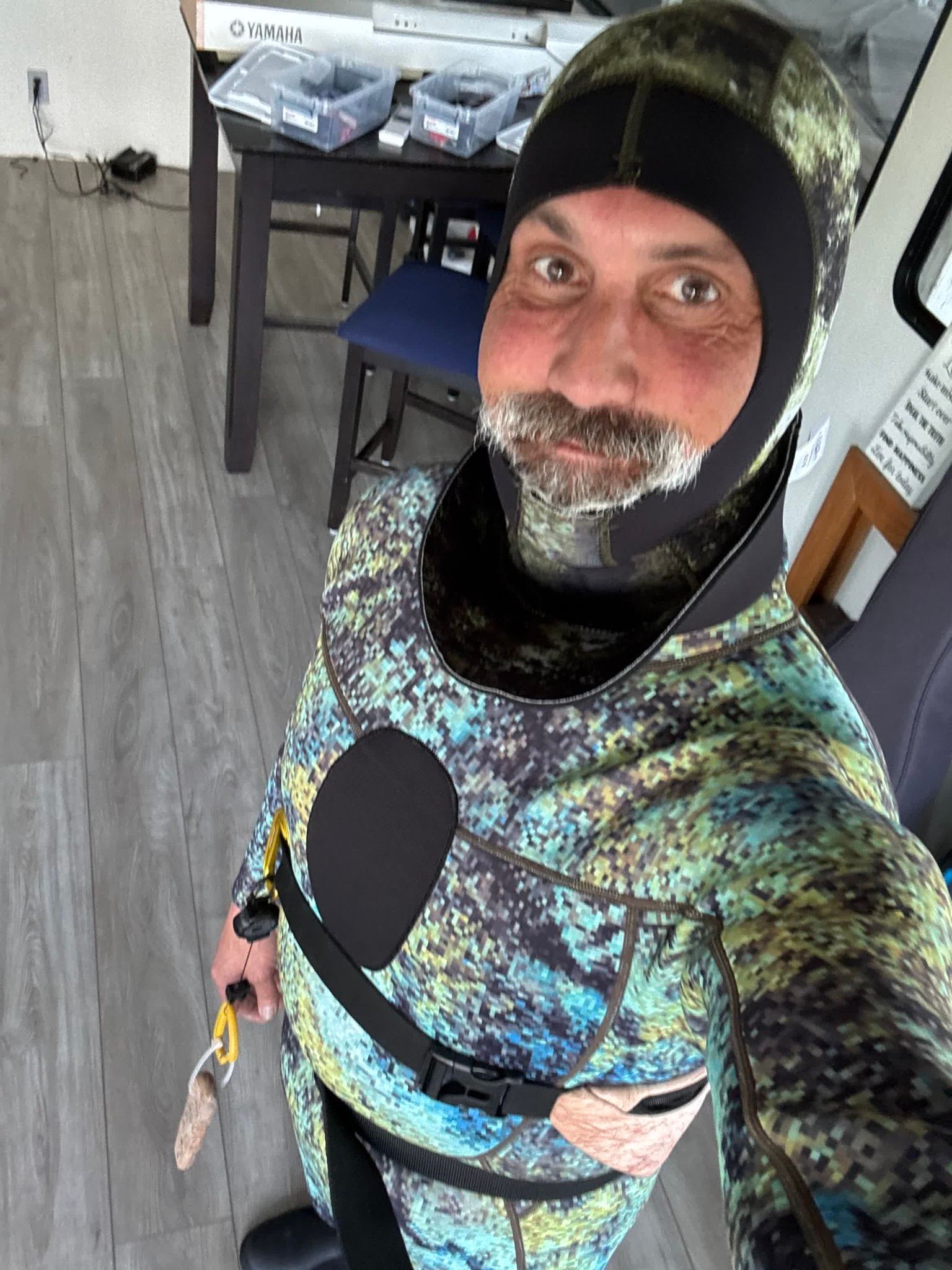 Man wearing a camouflage wetsuit indoors, smiling at the camera.
