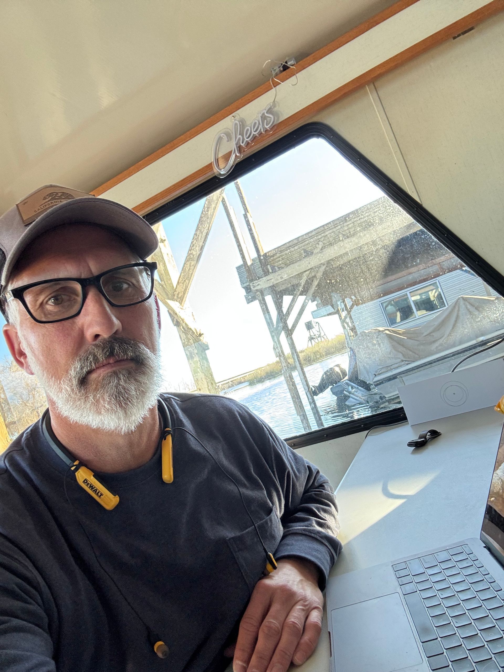 Man with glasses and a beard in a boat, looking at the camera. Sunlight streams through the window.