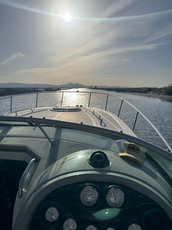 Boat navigating a waterway on a sunny day. Sun reflection on the water, mountains in the distance.