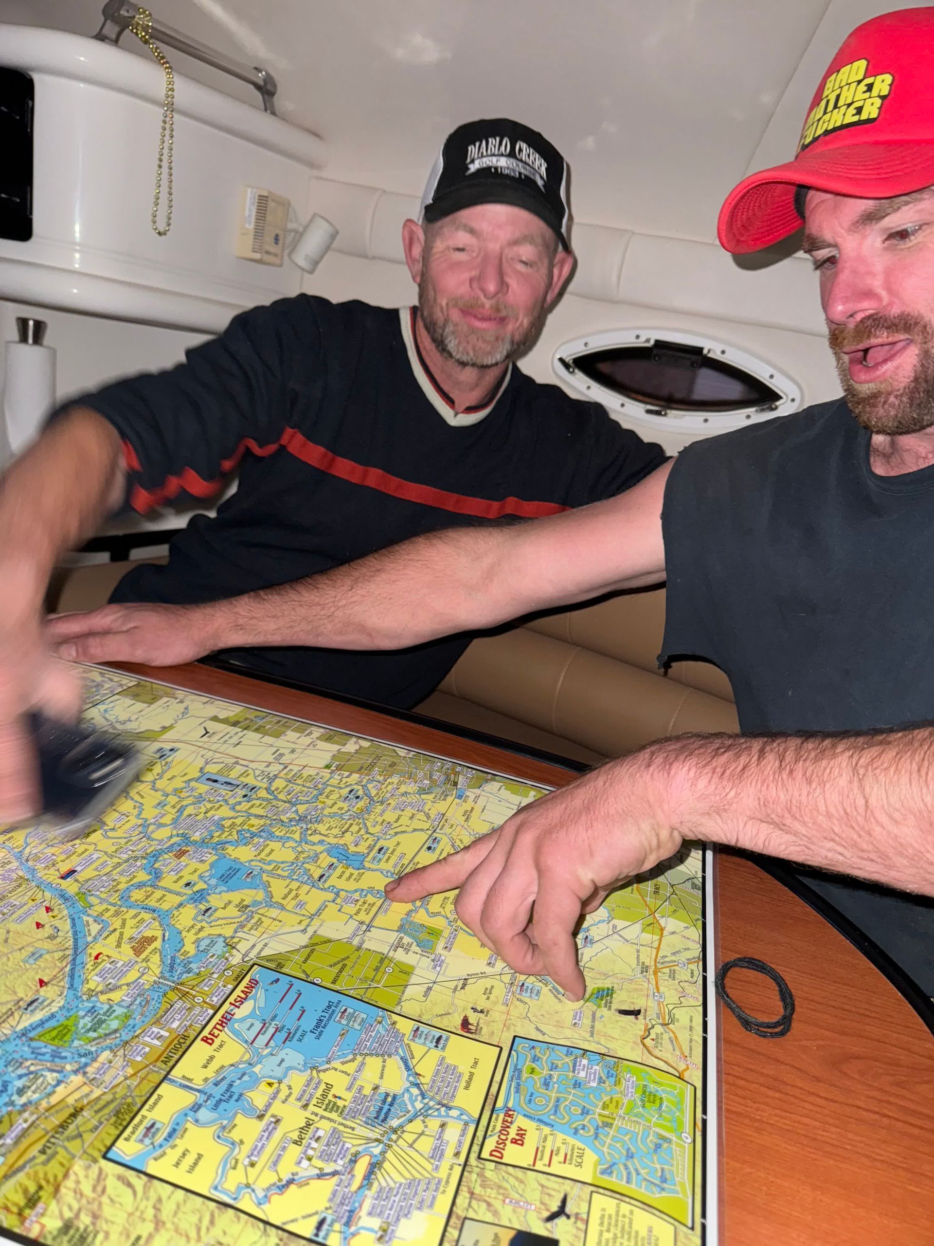 Two men on a boat looking at a nautical chart. One points, both wear hats.