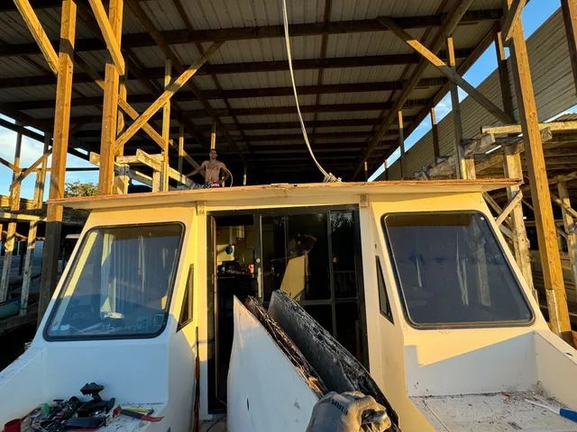 Boat under a wooden shelter, person working on its roof, light shining through the structure.