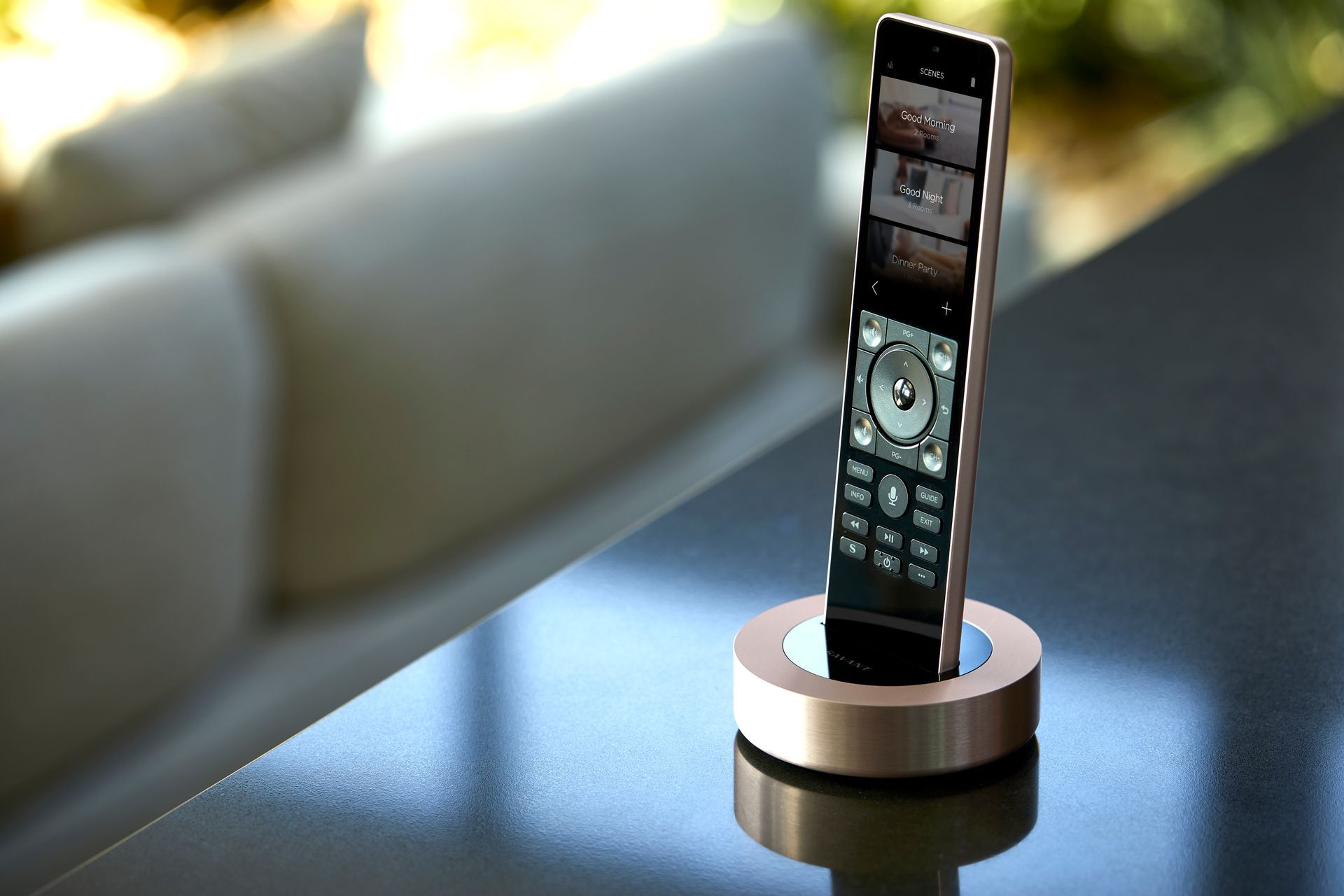 Remote control standing in a rose gold dock on a dark surface, with a couch in the blurred background.