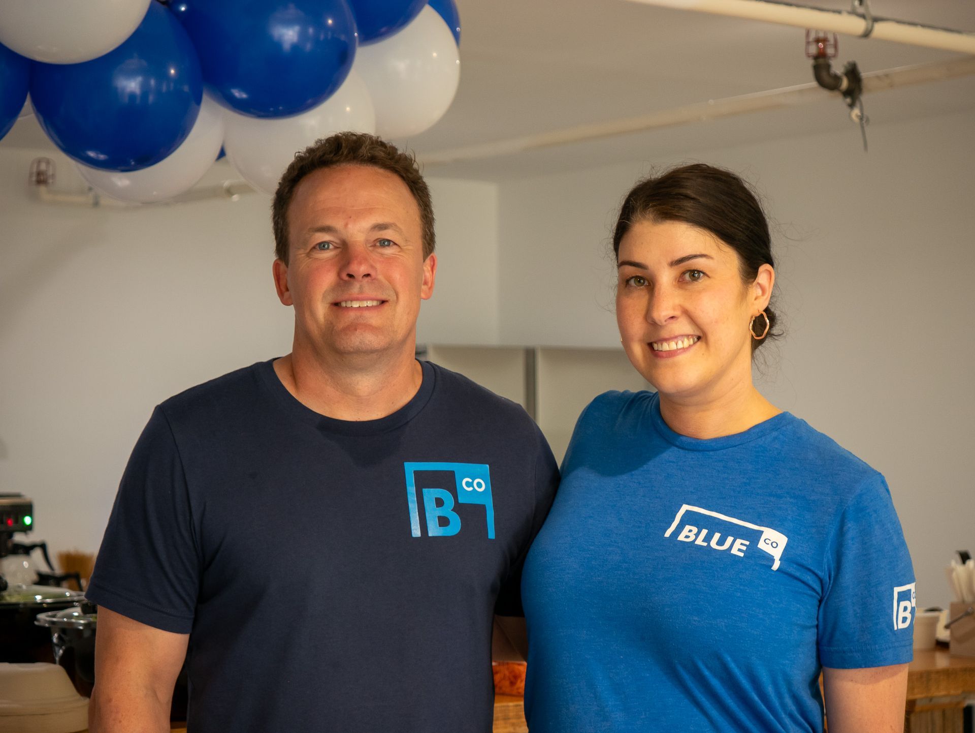 Two people doing yoga outside. One in pink, one in white, arms outstretched, smiling.