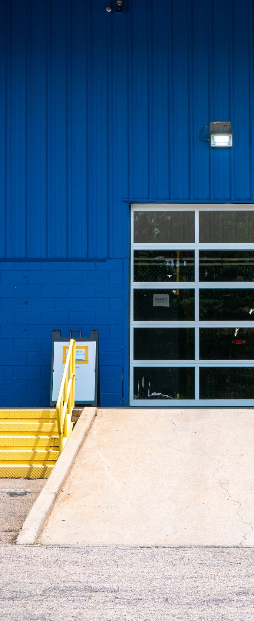 Outdoor patio with light gray couches, white pergola, blue-trimmed windows, and stone floor.