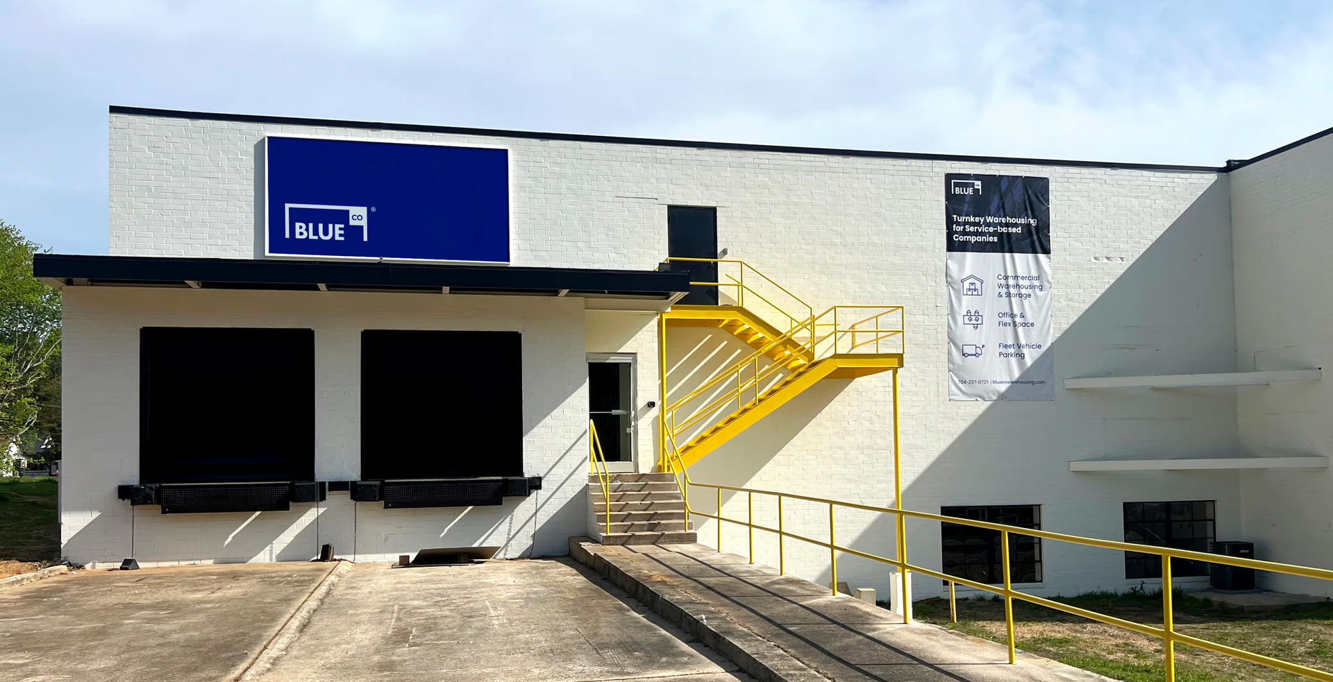 Outdoor patio with light gray couches, white pergola, blue-trimmed windows, and stone floor.