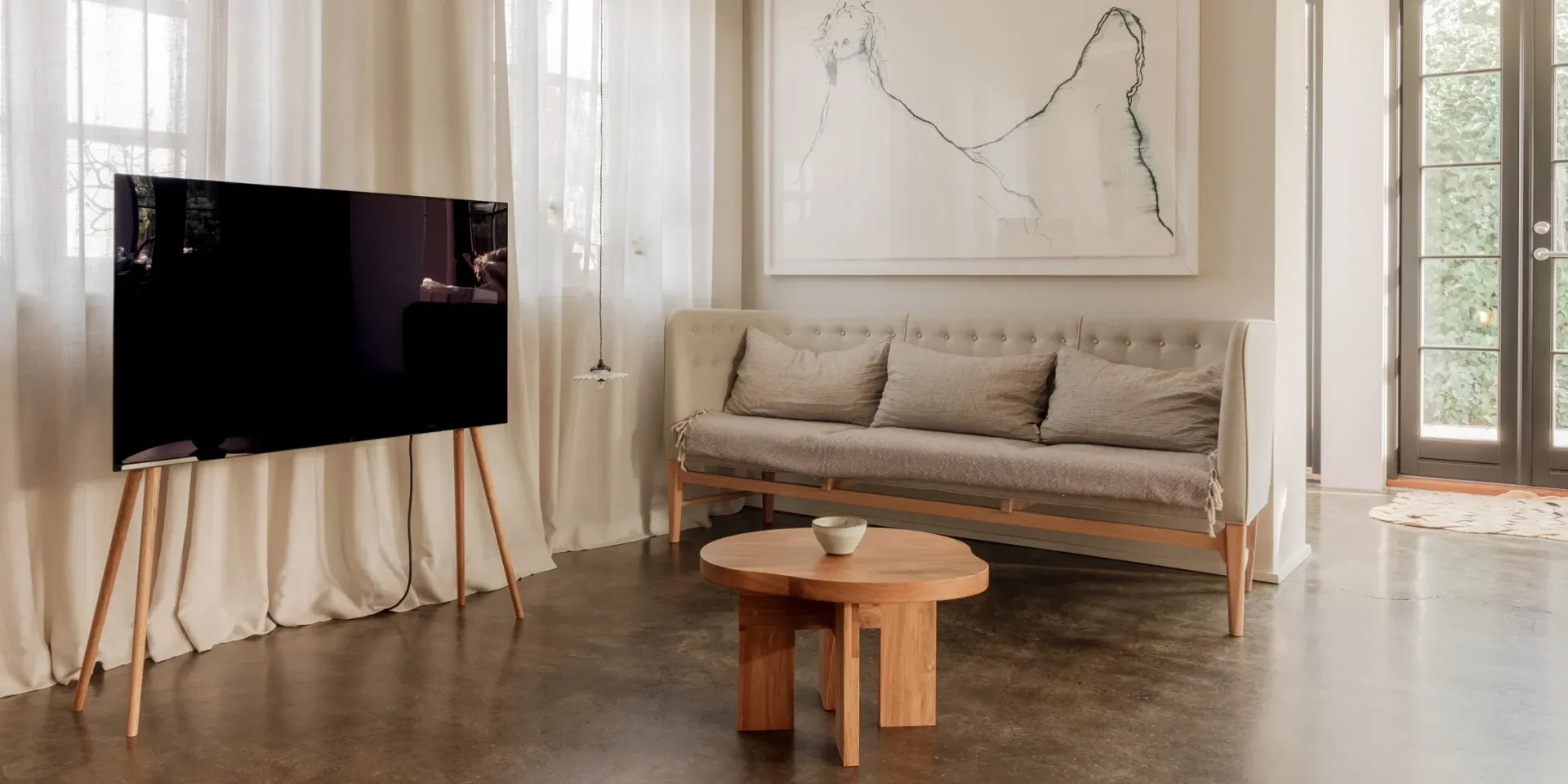 Living room with a large black TV on a wooden stand, a light-colored sofa, and a round wooden coffee table.