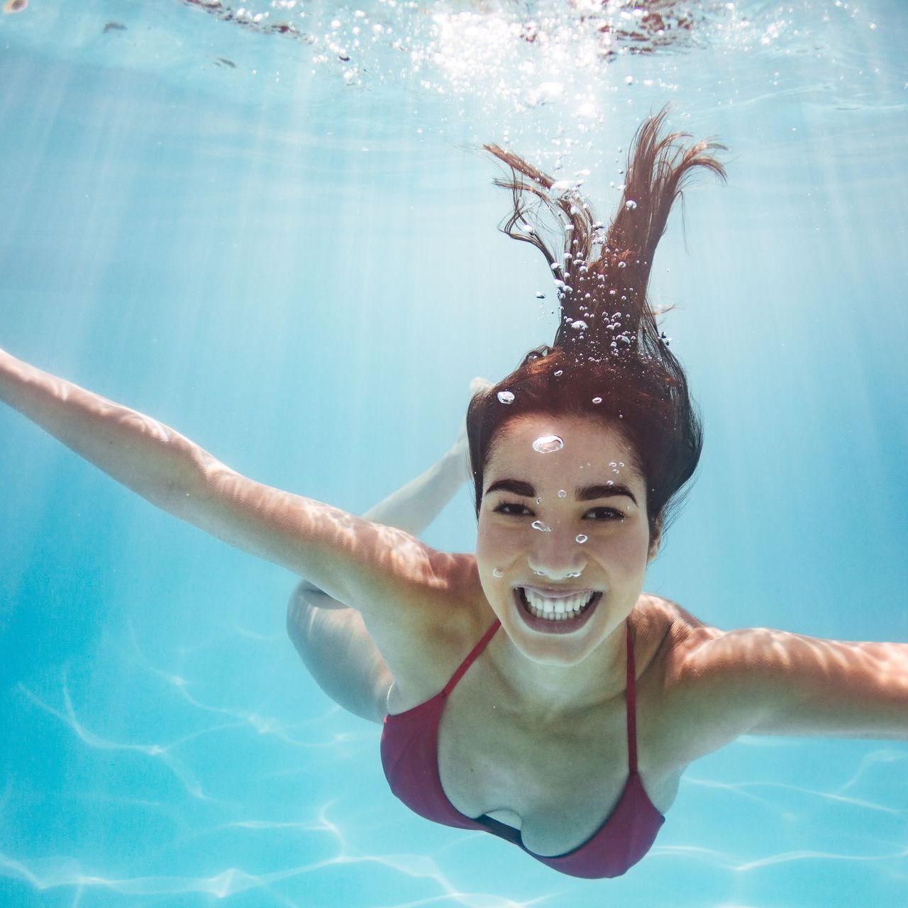 A woman in a red bikini is swimming underwater and smiling