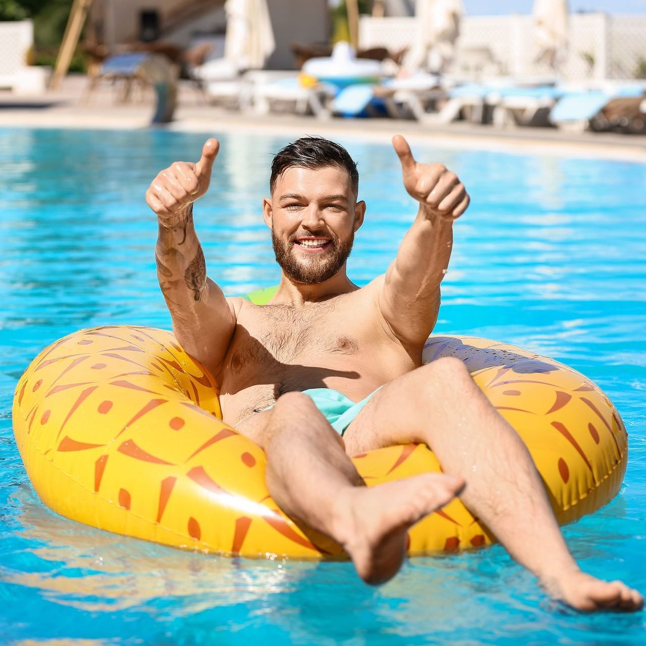 A man is floating on an inflatable donut in a swimming pool and giving a thumbs up.