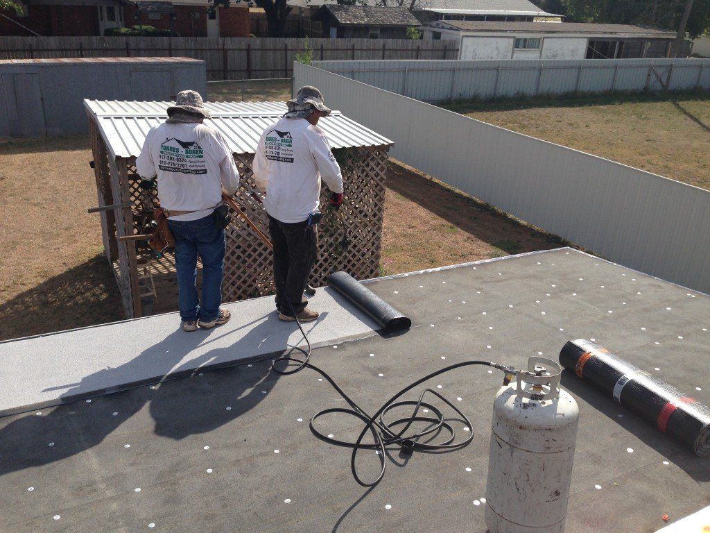 two men are working on a roof with a roofing company on their shirts