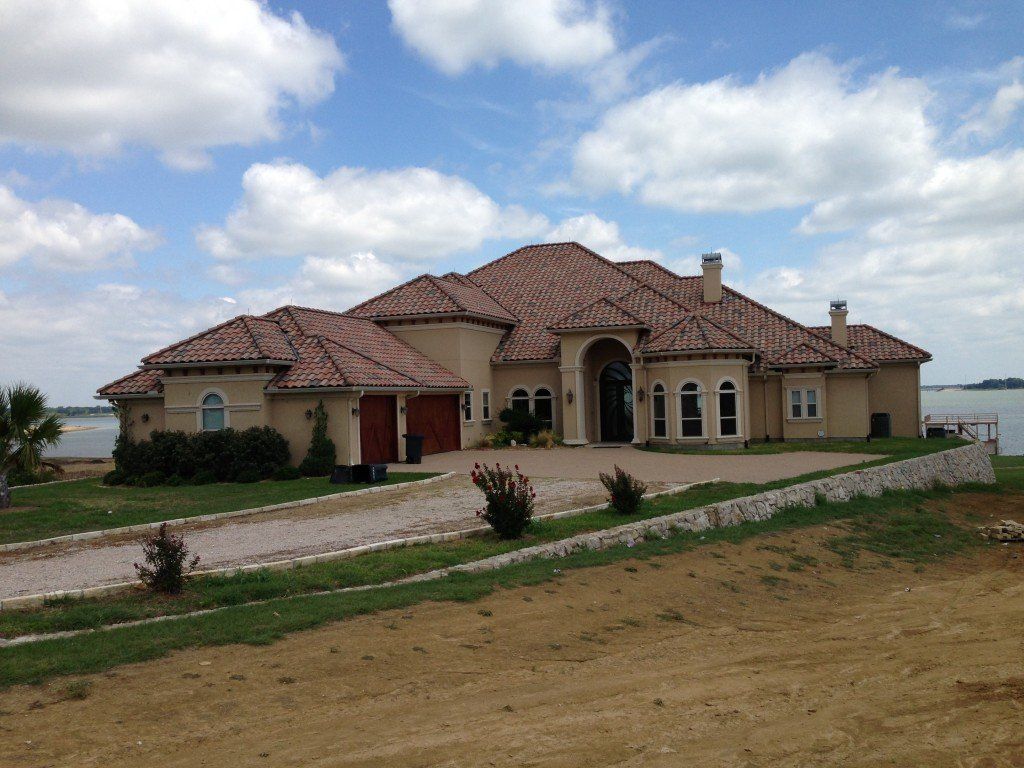 a large house with a tiled roof sits next to a body of water